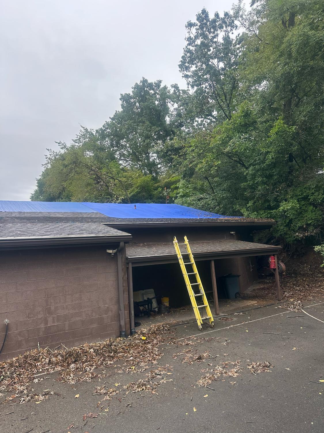 Blue emergency tarp secured over a storm-damaged roof on a block building